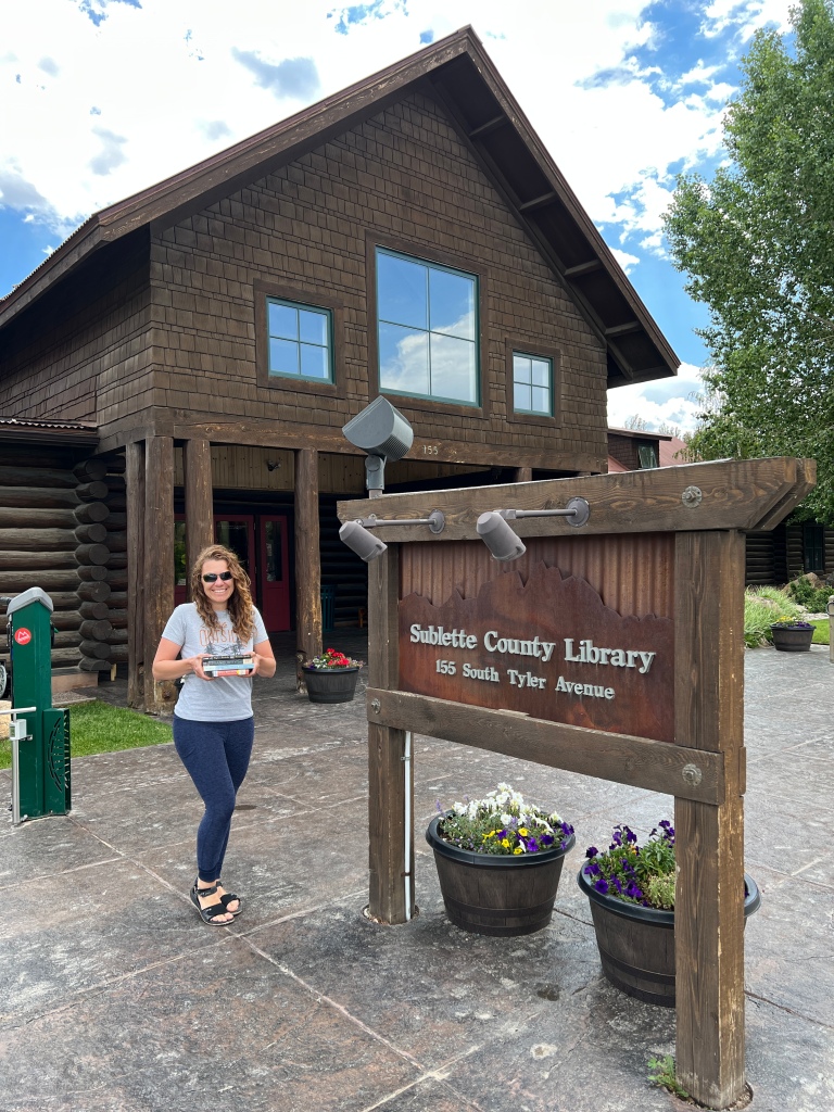 Agnes in front of Sublette County Library with a stack of books.